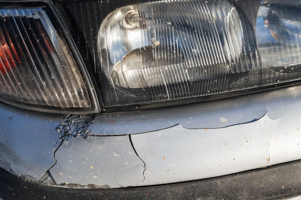 Nahaufnahme der Frontstoßstange eines Autos mit sichtbaren Makeln wie Rissen und Kratzern unterhalb des Scheinwerfers