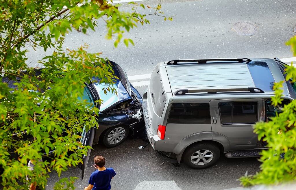 Zwei Fahrzeuge stehen nach einem Auffahrunfall auf einer Straße, grüne Blätter umrahmen die Szene, eine Person steht in der Nähe