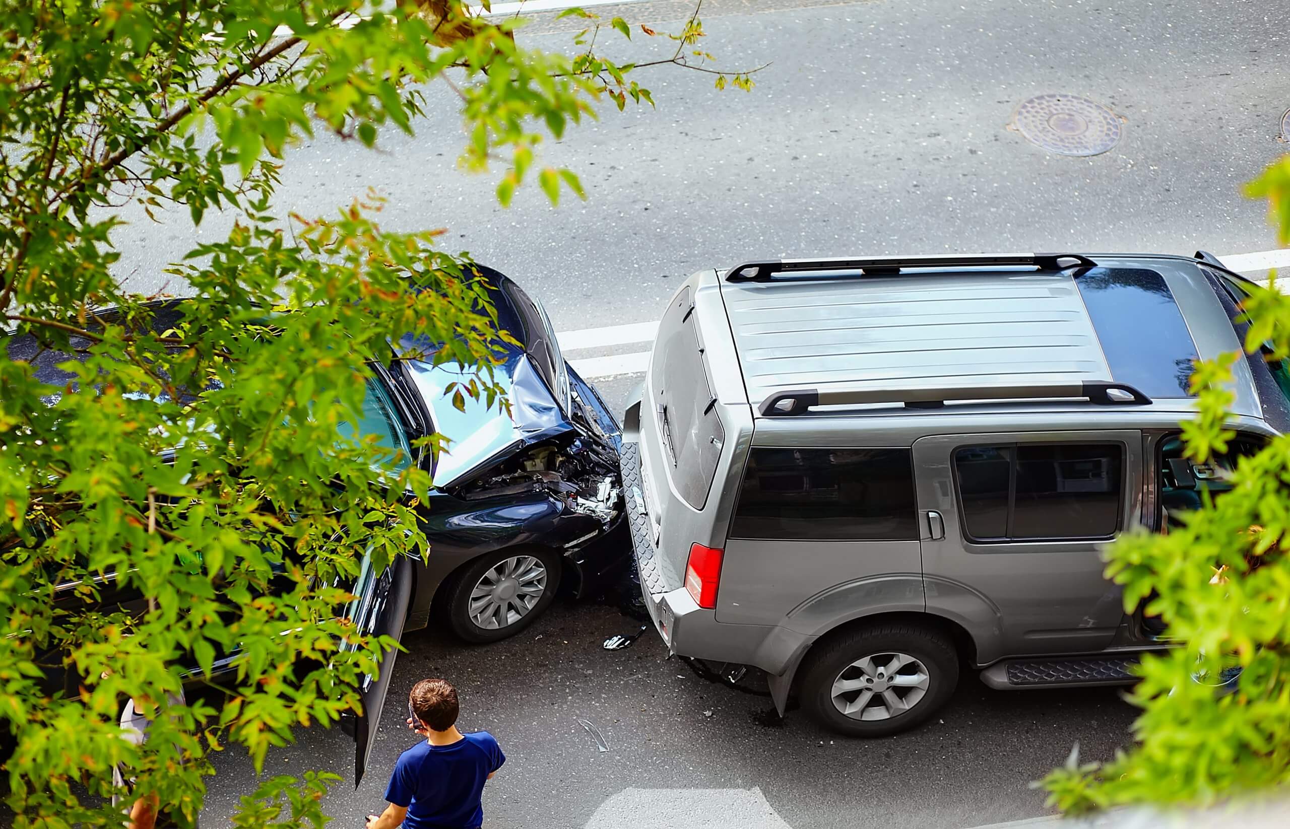 Zwei Fahrzeuge stehen nach einem Auffahrunfall auf einer Straße, grüne Blätter umrahmen die Szene, eine Person steht in der Nähe