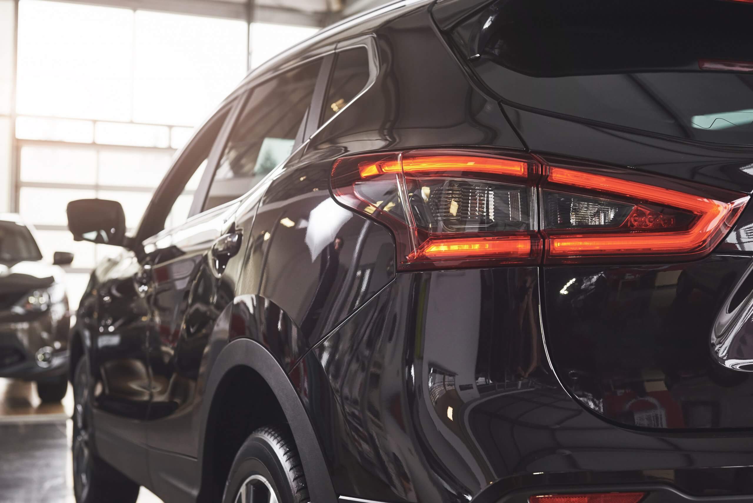 Nahaufnahme des Hecks eines schwarzen SUV mit eingeschaltetem Rücklicht, geparkt im Showroom Automatisch gespeicherter Entwurf