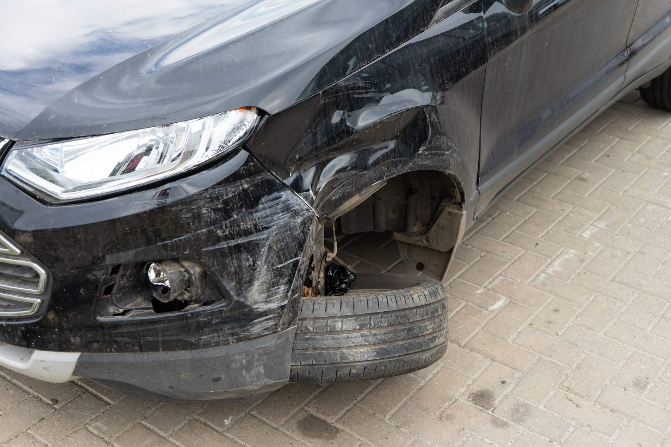 Ein schwarzes Auto mit beschädigter linker Front, fehlendem Rad und verbogenem Reifen steht als automatisch gespeicherter Entwurf
