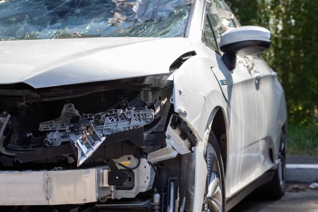 Ein silbernes Auto mit zerstörter Front und zerbrochener Windschutzscheibe steht neben Grünfläche