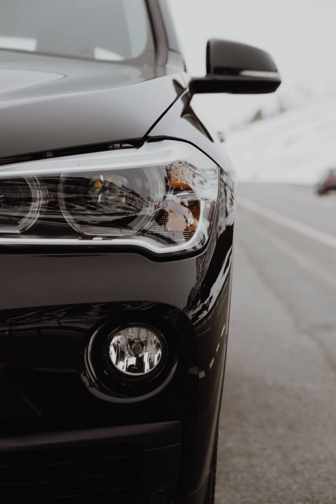 Nahaufnahme des linken Scheinwerfers und Kühlergrills eines schwarzen Autos mit automatisch gespeichertem Entwurf im verschneiten Hintergrund