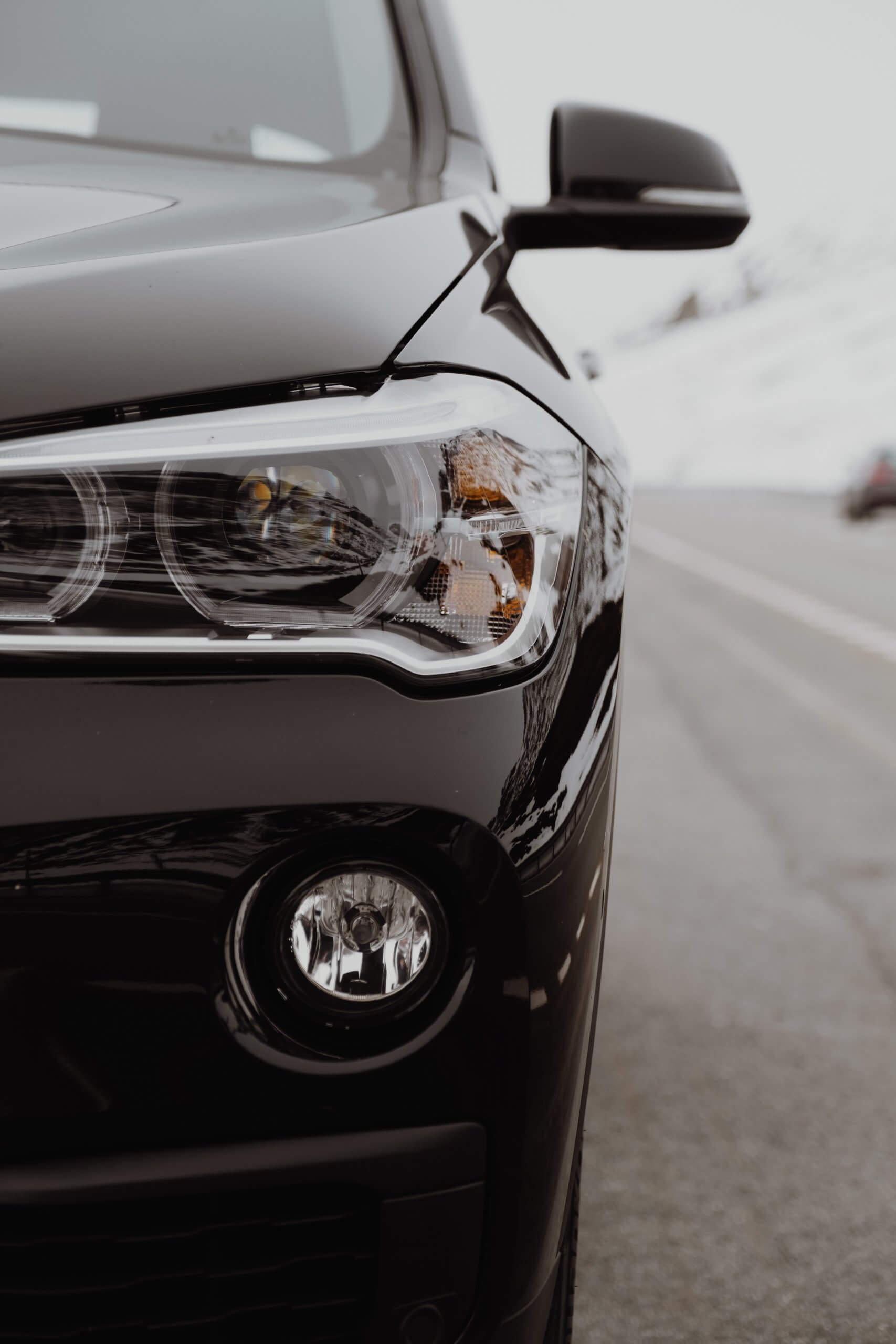 Nahaufnahme des linken Scheinwerfers und Kühlergrills eines schwarzen Autos mit automatisch gespeichertem Entwurf im verschneiten Hintergrund
