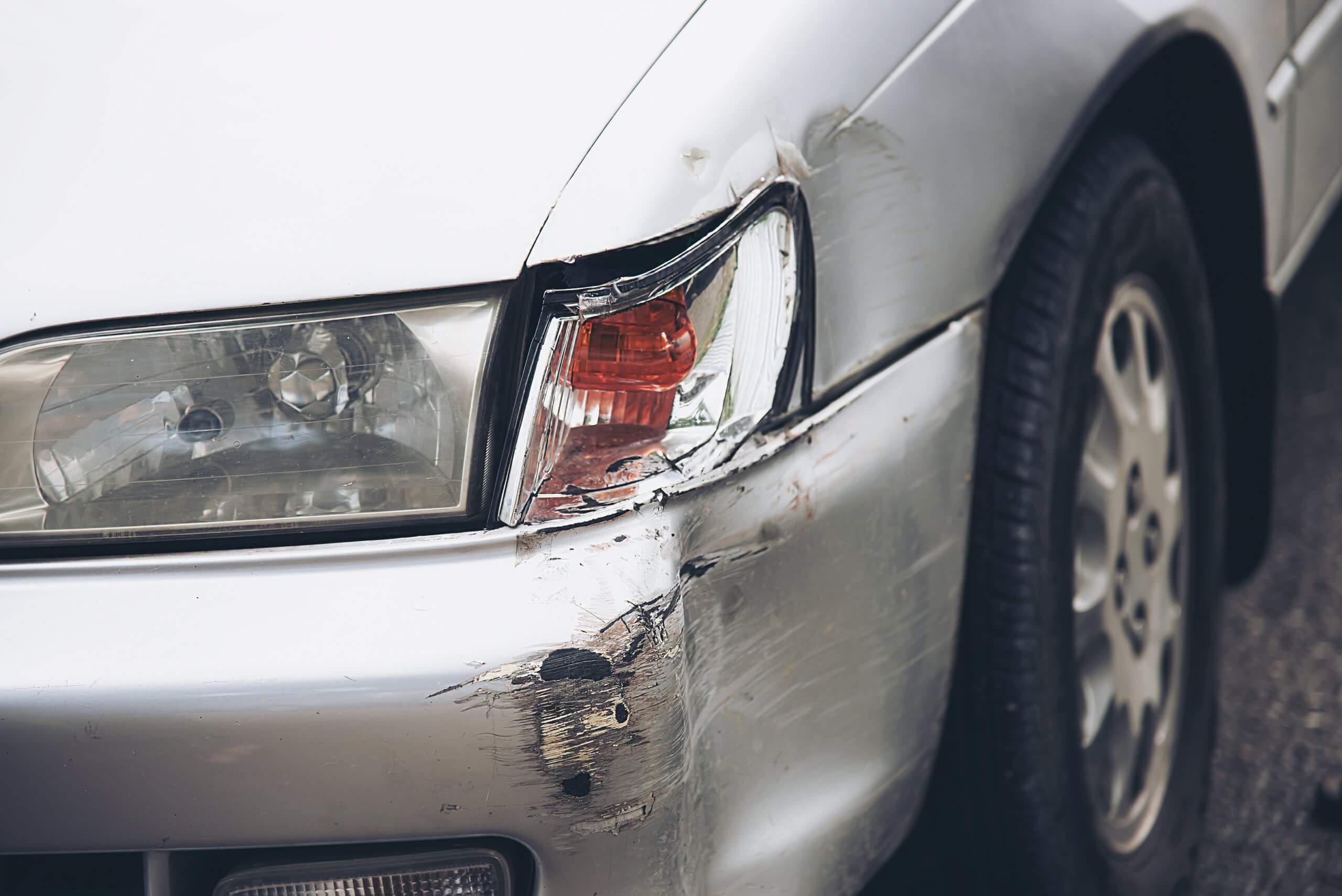 Silbernes Auto mit beschädigter Frontstoßstange, Kratzern im Lack und Reparaturkostenkalkulation am Fahrerseiten-Scheinwerfer