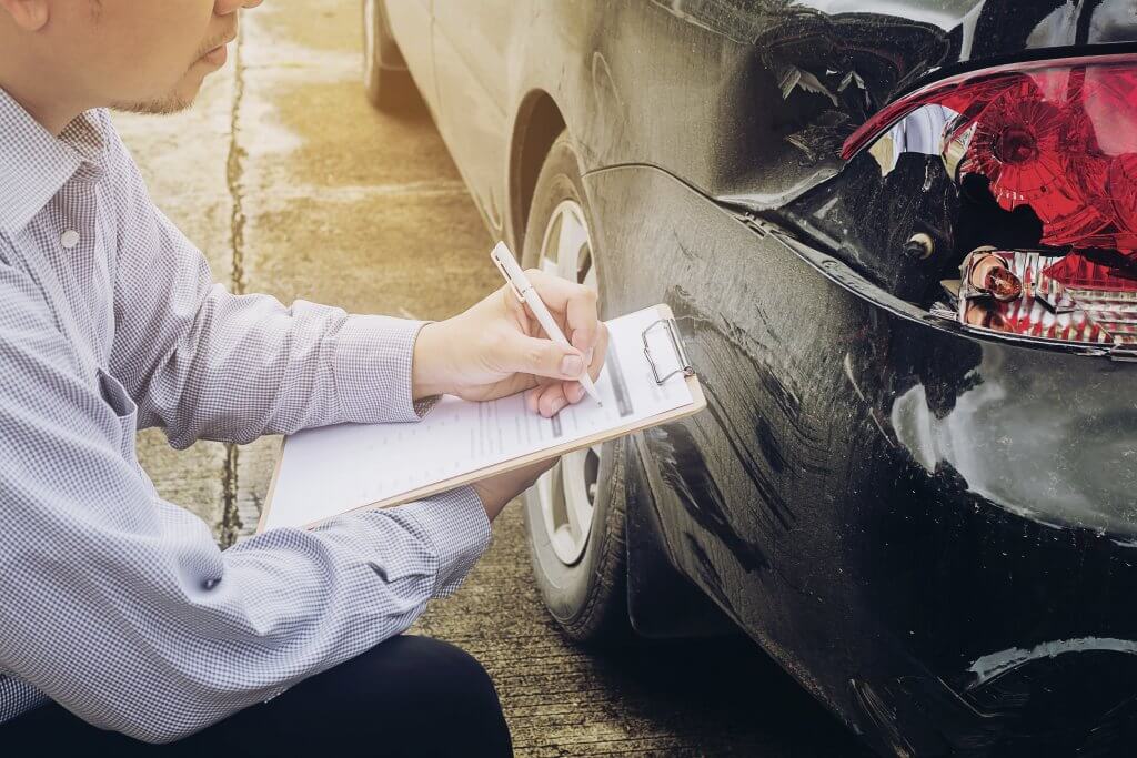Eine Person hält ein Klemmbrett und begutachtet den Heckschaden zur Reparaturkostenkalkulation an einem schwarzen Auto